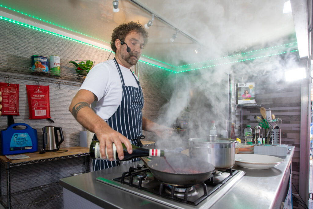 Nick Rowberry performing a cooking demo at the Stratford upon Avon Food Festival. He's pouring wine into a hot pan, creating a lot of atmospheric steam you can smell through the photo